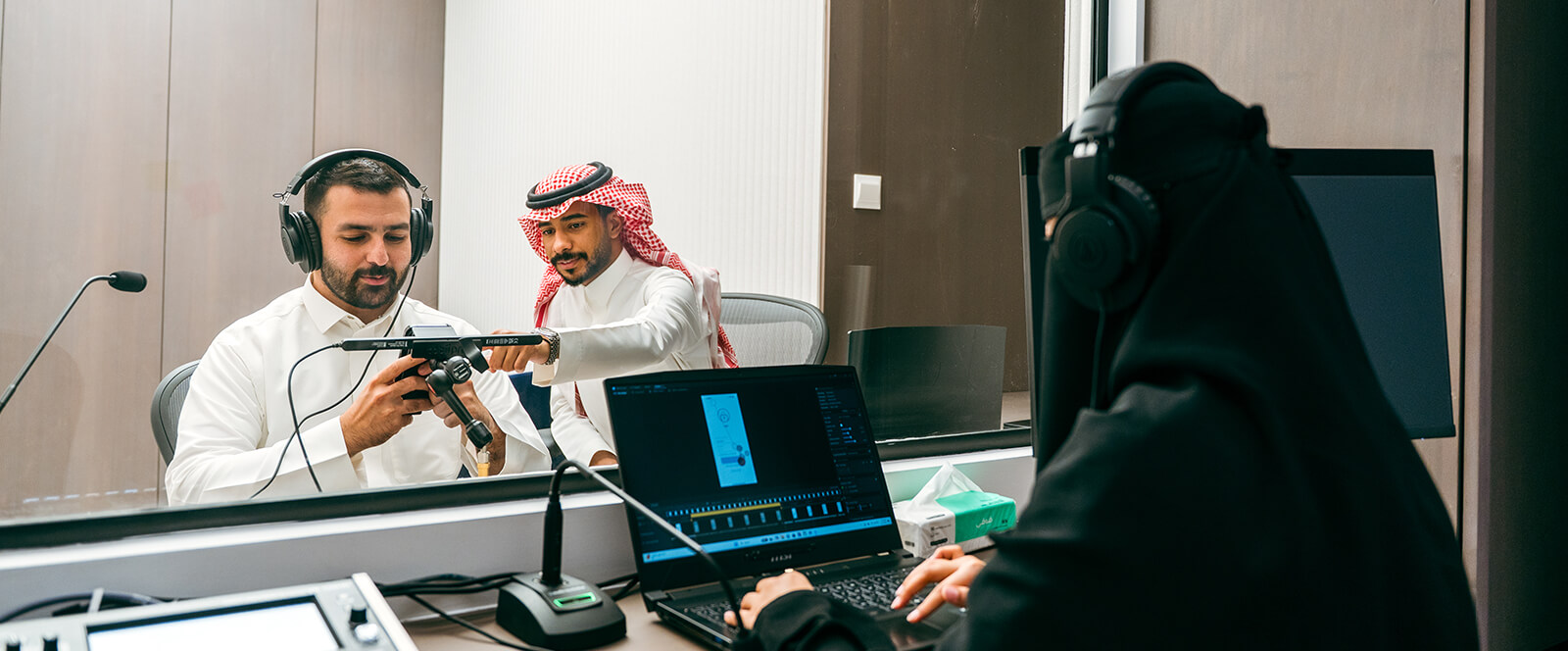Moderator adjusts smartphone eye-tracking rig for participant while researcher observes from control room laptop.